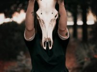 person wearing black dress while holding skull mask with horns
