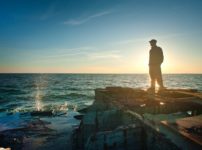 silhouette photo of man standing near the edge of concrete pavement